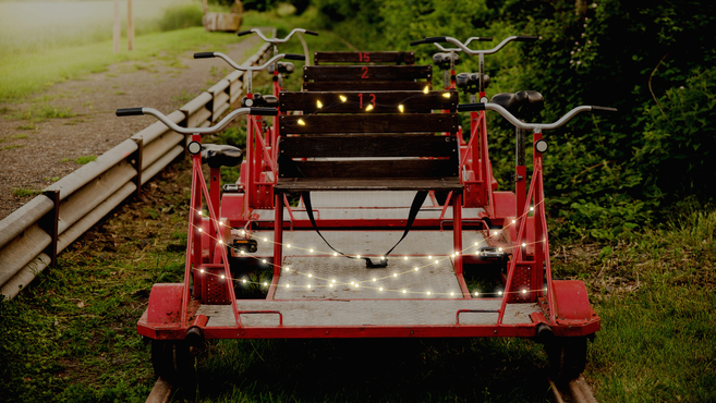 Eine rote Draisine mit Lichterketten geschmückt auf einem Gleis im Grünen.