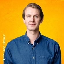 Ein Mann in einem blauen Hemd vor einem orangefarbenen Hintergrund.