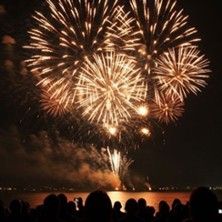 Feuerwerk über dem Meer bei Nacht mit Zuschauern im Vordergrund.