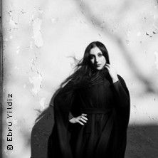 Schwarz-weiß Foto einer Frau in einem langen Kleid vor einer Wand.