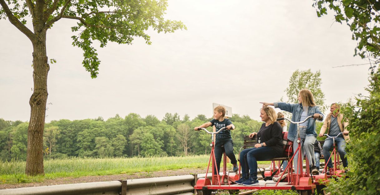 Eine Gruppe von Menschen fährt auf einer roten Draisine entlang einer grünen Landschaft.
