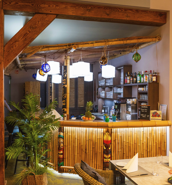 Innenansicht einer Tiki-Bar mit Bambusdekor und tropischen Pflanzen.