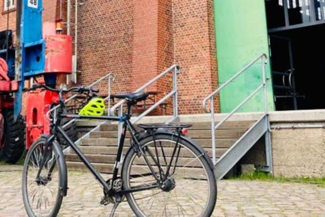 Ein Fahrrad steht vor einem Backsteingebäude mit grüner Tür und Treppe.