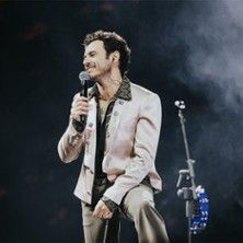 Ein Sänger in einem eleganten Anzug hält ein Mikrofon auf einer Bühne.