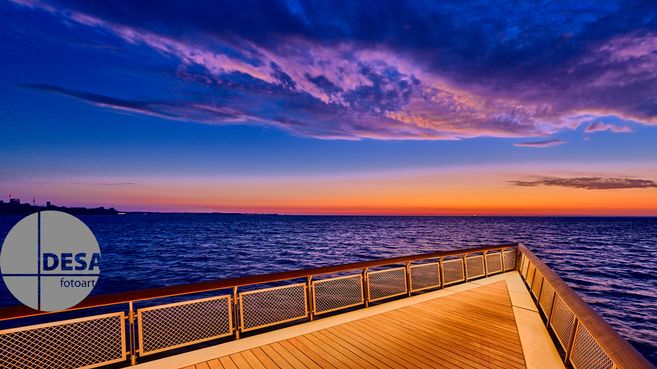 Eine Seebrücke erstreckt sich über das Meer bei Sonnenaufgang, mit einem farbenfrohen Himmel im Hintergrund.