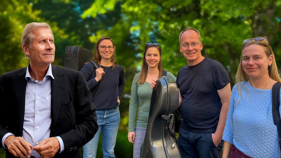 Fünf Personen stehen im Freien, einige halten Instrumentenkoffer. Hintergrund ist grün und unscharf.
