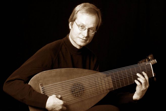 Ein Mann spielt eine Laute vor einem dunklen Hintergrund.