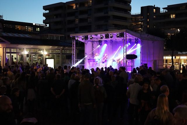 Menschenmenge vor einer beleuchteten Bühne bei einer Abendveranstaltung im Freien.