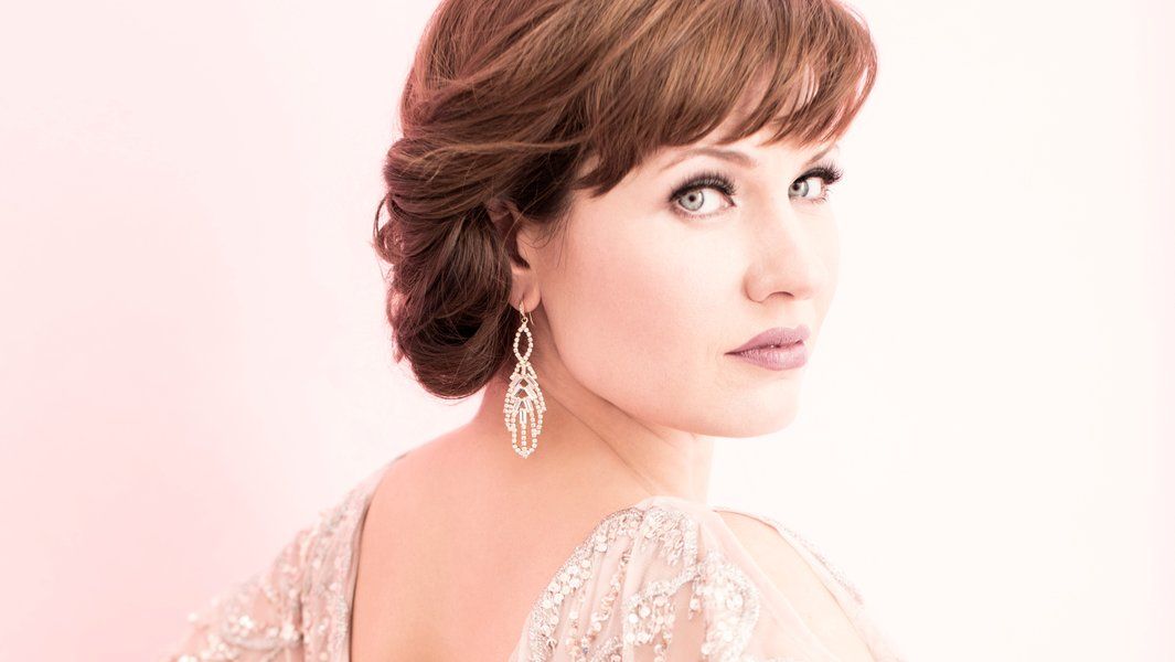 Porträt einer Frau mit eleganter Frisur und funkelnden Ohrringen vor einem rosa Hintergrund.