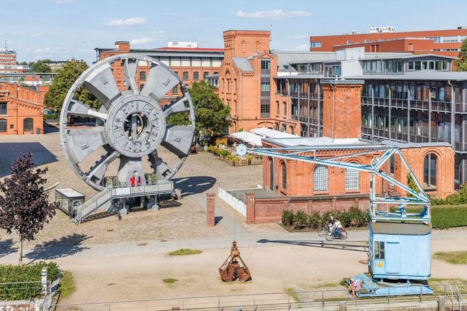 Großes Schaufelrad und historische Backsteingebäude im Freilichtmuseum mit Besuchern.