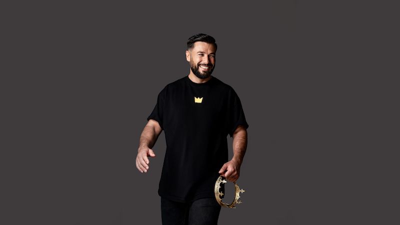 Mann in schwarzem T-Shirt mit Krone-Logo hält eine goldene Krone in der Hand.