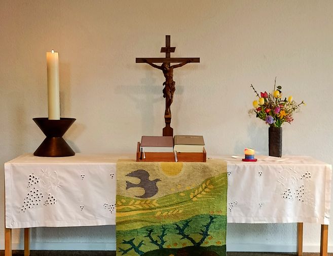 Ein Altar mit einer Kerze, einem Kruzifix, Blumen und Büchern.