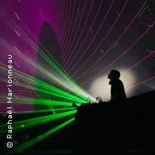 Ein DJ steht vor einer beeindruckenden Lichtshow mit grünen und violetten Lasern.