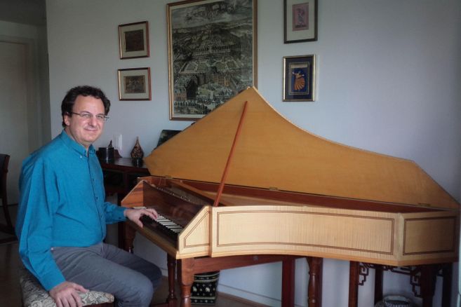 Ein Mann sitzt an einem historischen Tasteninstrument in einem Raum mit dekorativen Wandbildern.