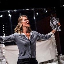 Eine Frau auf einer Bühne hält ein Schwarz-Weiß-Foto hoch.