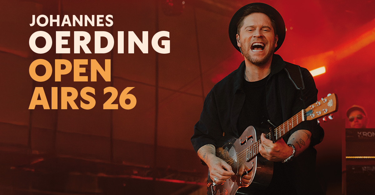 Musiker spielt Gitarre auf der Bühne mit rotem Hintergrund.