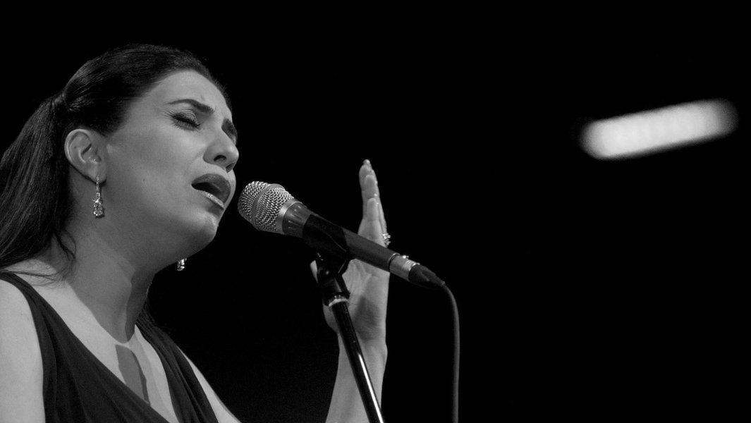 Eine Frau singt leidenschaftlich in ein Mikrofon auf einer Bühne.