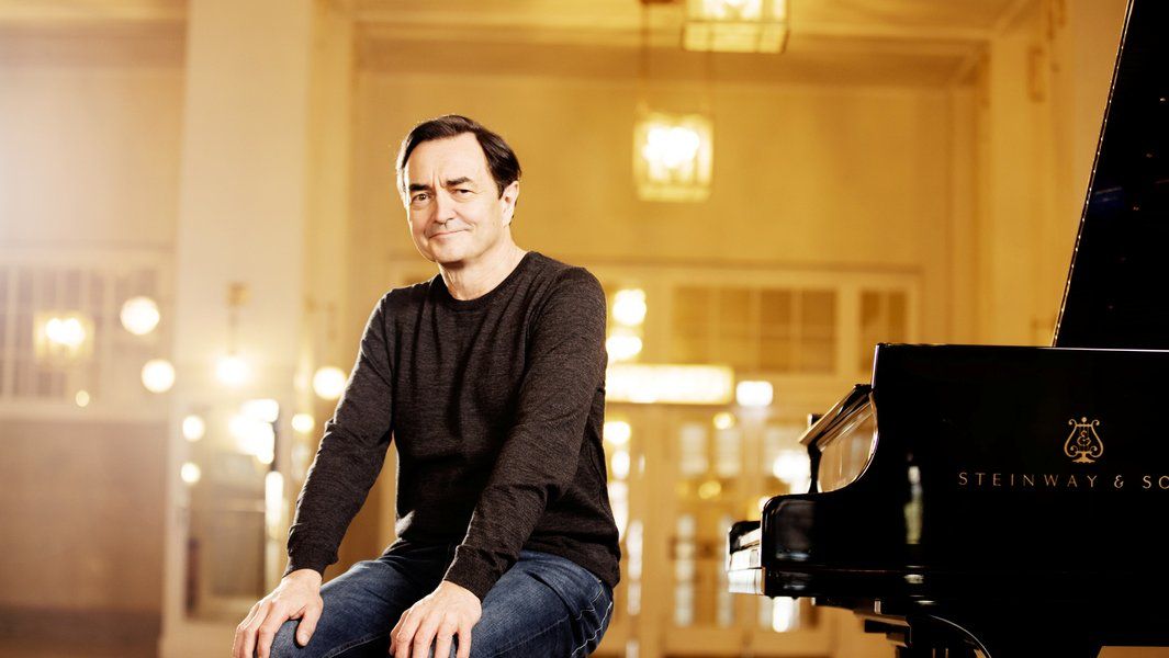 Ein Mann sitzt neben einem Steinway & Sons Flügel in einem elegant beleuchteten Raum.