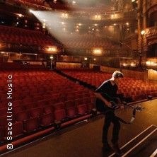 Musiker mit Gitarre auf einer leeren Theaterbühne.