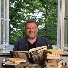 Ein Mann sitzt vor einem offenen Fenster mit Büchern auf einem Tisch.