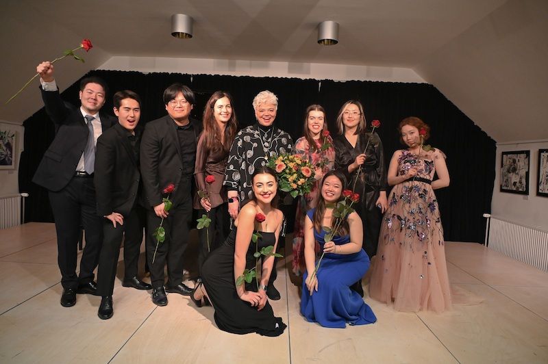 Gruppe von Menschen in Abendkleidung auf einer Bühne mit Rosen.