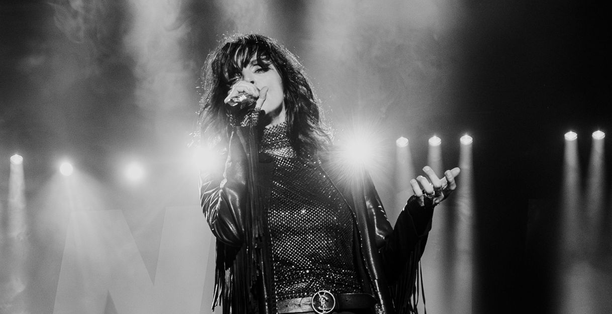 Schwarz-weiß Foto einer Sängerin auf der Bühne mit Mikrofon und Lederjacke.