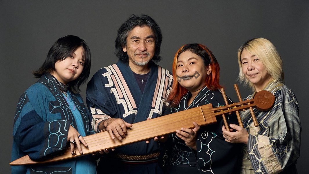 Vier Personen in traditioneller Kleidung posieren mit einem Musikinstrument.