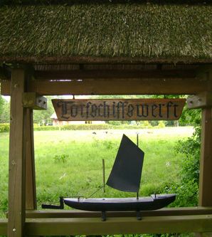Holzschild mit der Aufschrift 'Torfschiffswerft' und einem Modell eines Torfschiffs darunter.