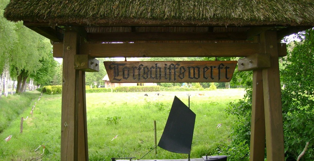 Holzschild mit der Aufschrift 'Torfschiffswerft' und einem Modell eines Torfschiffs darunter.