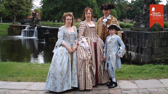 Eine Familie in historischen Kostümen steht vor einem Brunnen im Freien.