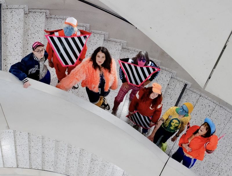 Gruppe von Menschen in bunter, auffälliger Kleidung auf einer Wendeltreppe von oben fotografiert.