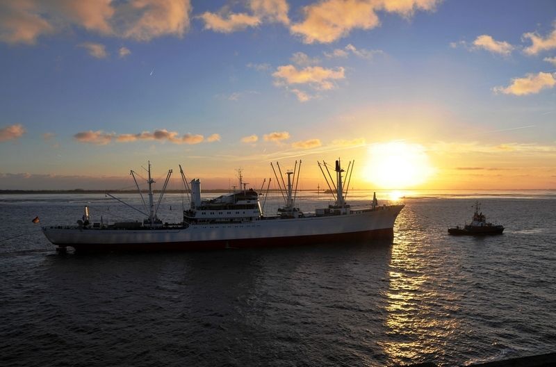 Ein großes Schiff und ein Schlepper im Hamburger Hafen bei Sonnenuntergang.