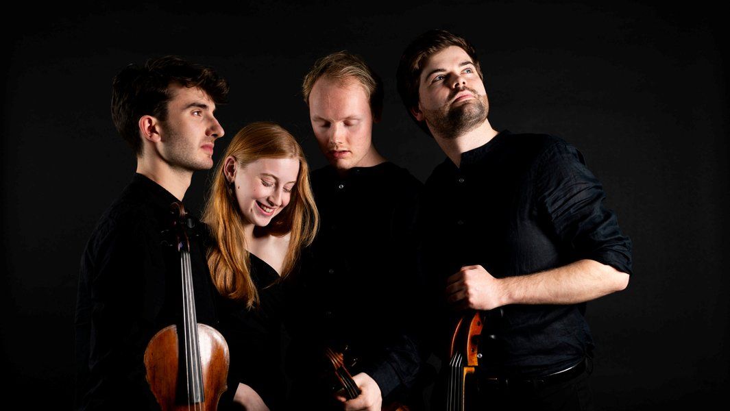 Vier Musiker in schwarzer Kleidung mit Streichinstrumenten vor schwarzem Hintergrund.