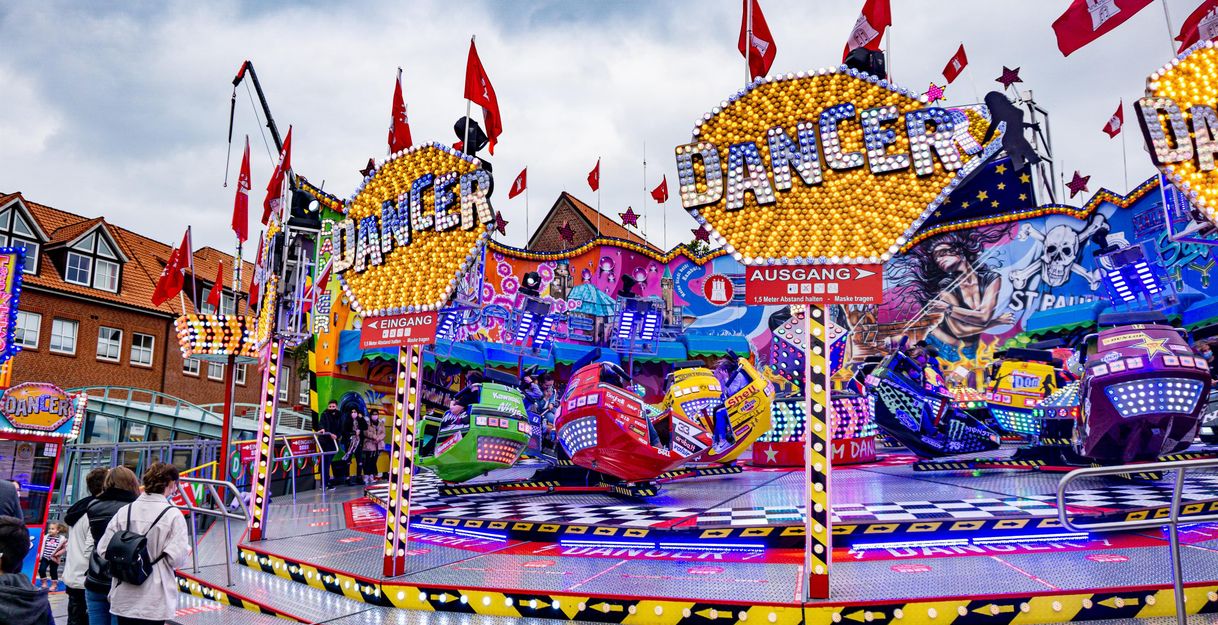 Bunte Kirmesattraktion mit leuchtenden Schildern und Fahrgeschäften, umgeben von Menschen und Fahnen.