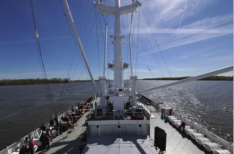 Schiff auf der Elbe mit Passagieren an Deck, blauer Himmel.