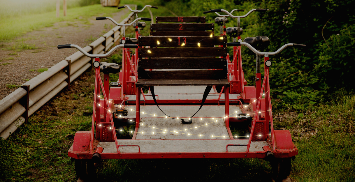 Eine rote Draisine mit Lichterketten geschmückt auf einem Gleis im Grünen.