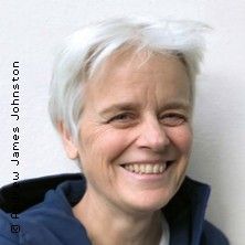 Porträt einer lächelnden Person mit kurzem, weißem Haar vor einem neutralen Hintergrund.