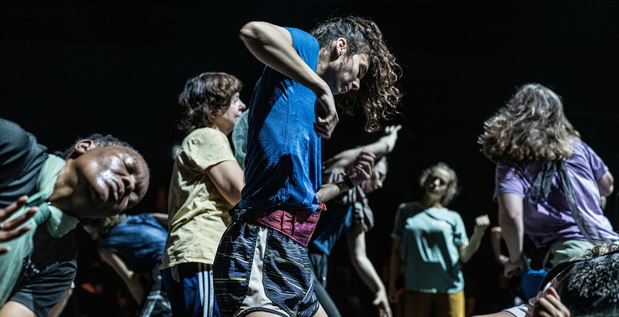 Dancers move intensely and expressively in a tight group formation on stage.