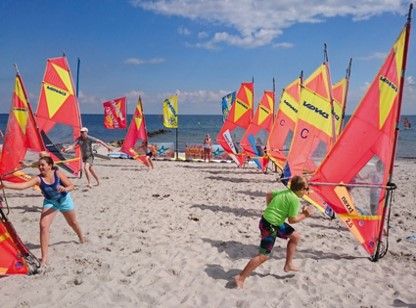Menschen üben Windsurfen am Strand mit bunten Segeln.