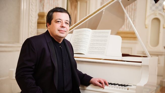 Ein Mann sitzt an einem weißen Flügel mit geöffnetem Notenblatt.