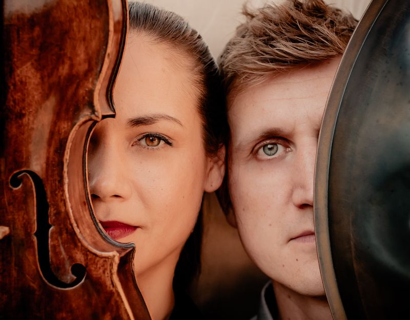 Nahaufnahme von zwei Personen, die jeweils ein Instrument vor ihr Gesicht halten: eine Geige und ein Becken.