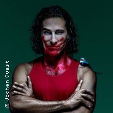 Ein Mann mit rotem Gesicht und rotem Tanktop, ein kleiner Vogel sitzt auf seiner Schulter.