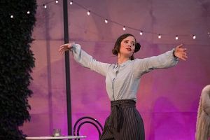 Eine Frau in einem Bühnenstück mit ausgestreckten Armen, im Hintergrund Lichterkette.