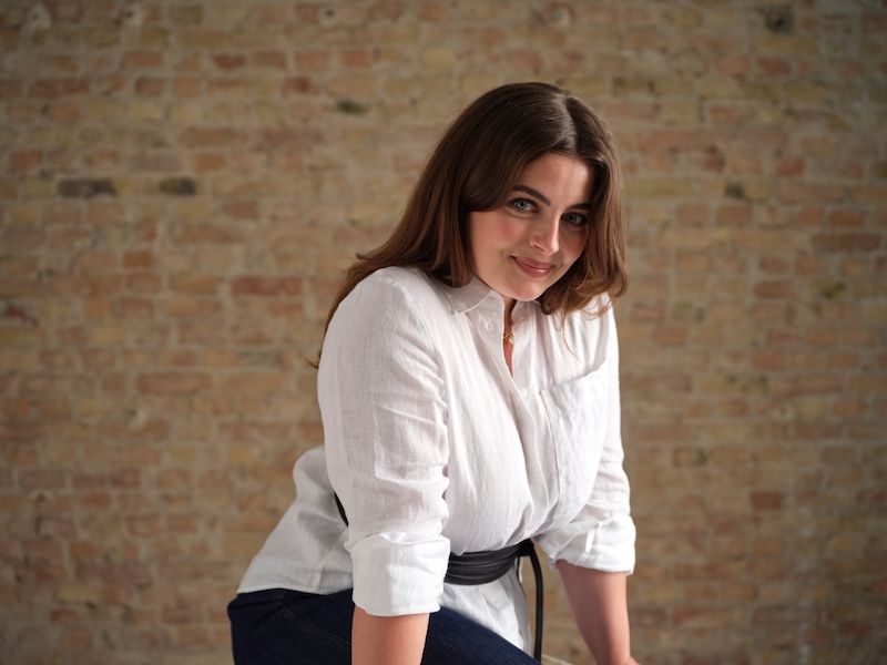 Eine Frau in weißem Hemd vor einer Backsteinwand.