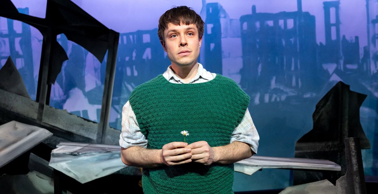 Ein junger Mann (Severin Mauchle) im grünen Pullunder, hält eine kleine weiße Blume in der Hand.