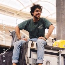 Ein Mann sitzt lächelnd auf einem großen Kasten in einer Halle.