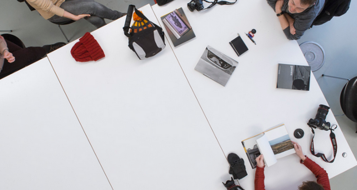 Menschen sitzen um einen Tisch mit Kameras und Fotobüchern.