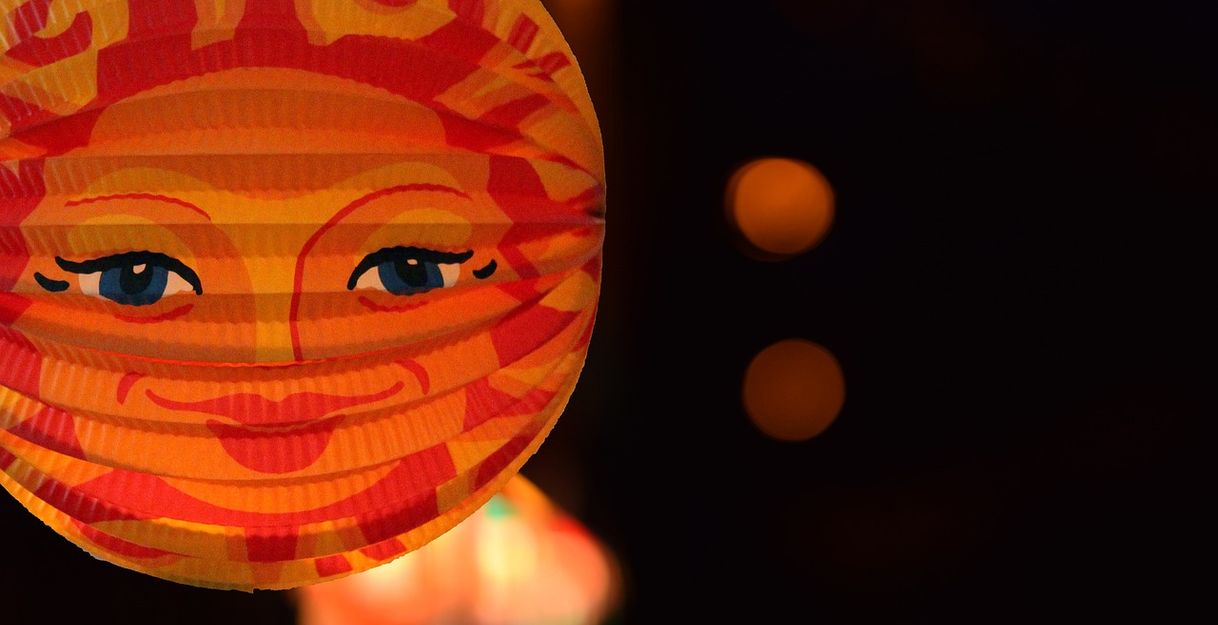 Bunte Papierlaterne mit Sonnenmotiv vor dunklem Hintergrund.