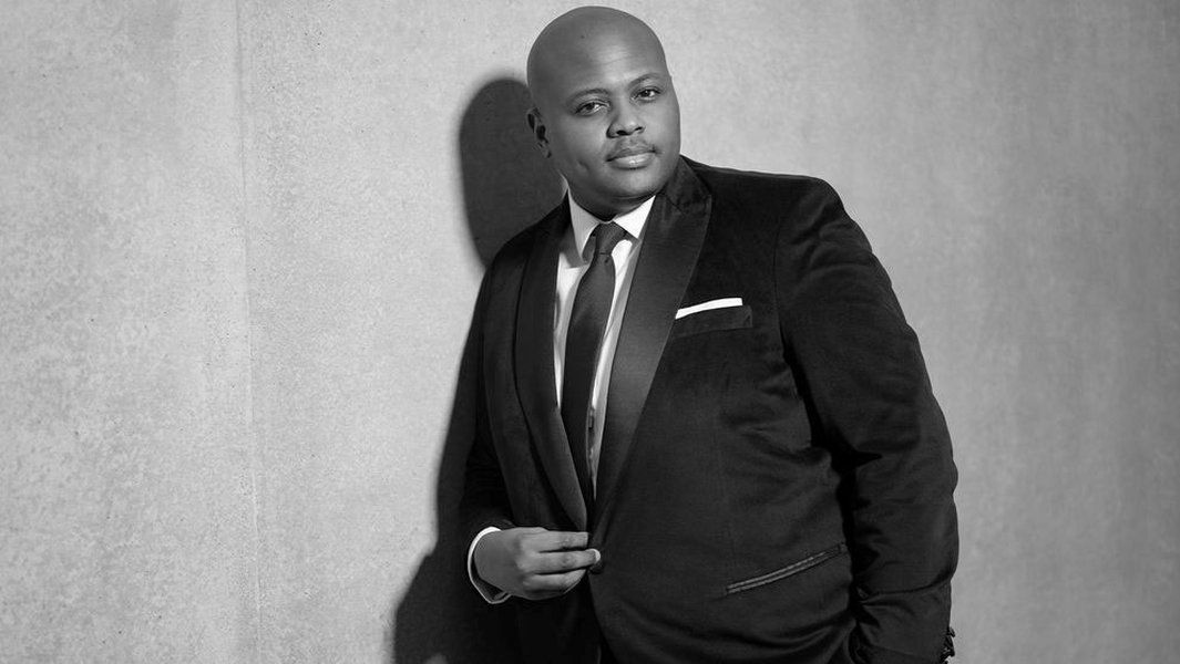 Schwarz-weiß Foto eines Mannes im Anzug, der an einer Wand lehnt.