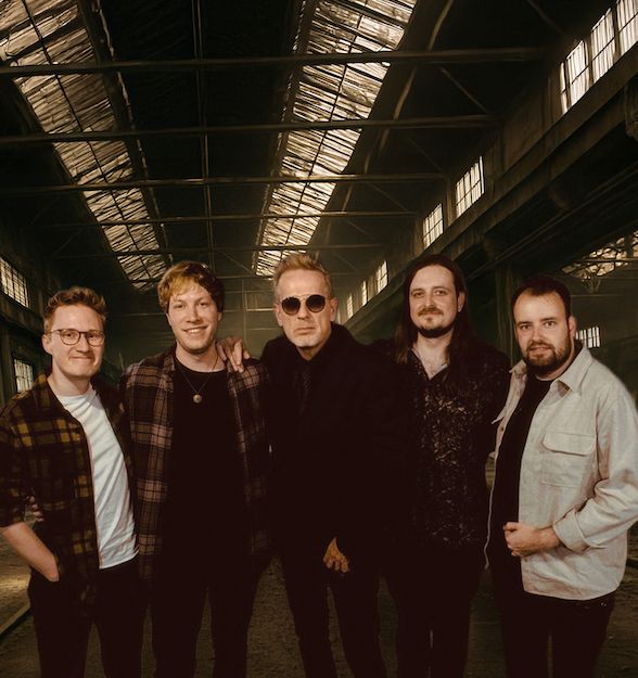 Fünf Männer stehen in einer alten Industriehalle und posieren für ein Foto.